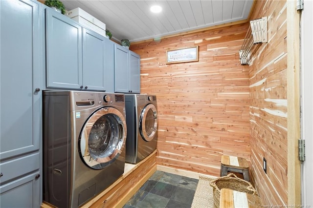 clothes washing area featuring cabinets, washer and clothes dryer, and wood walls