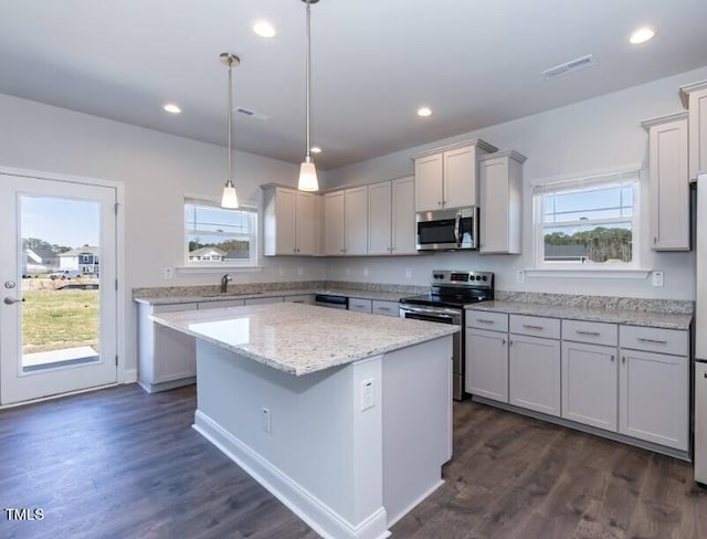 kitchen with decorative light fixtures, dark hardwood / wood-style flooring, a kitchen island, a wealth of natural light, and stainless steel appliances