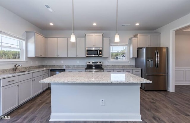 kitchen with appliances with stainless steel finishes, sink, hanging light fixtures, a center island, and light stone counters