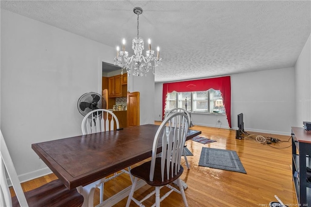 dining space with an inviting chandelier, a textured ceiling, and light wood-type flooring