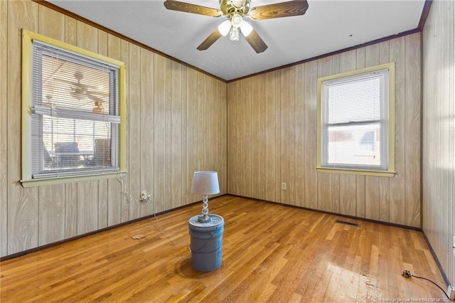 unfurnished room with crown molding, wooden walls, light wood-type flooring, and a wealth of natural light