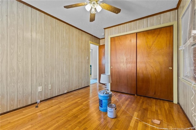 unfurnished bedroom with crown molding, ceiling fan, wood-type flooring, a closet, and wood walls