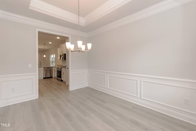 unfurnished room with ornamental molding, light wood-type flooring, a chandelier, and a tray ceiling