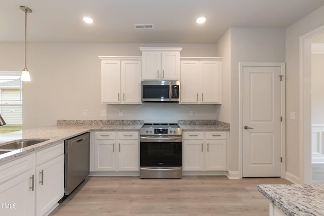 kitchen featuring light hardwood / wood-style flooring, appliances with stainless steel finishes, white cabinetry, hanging light fixtures, and kitchen peninsula