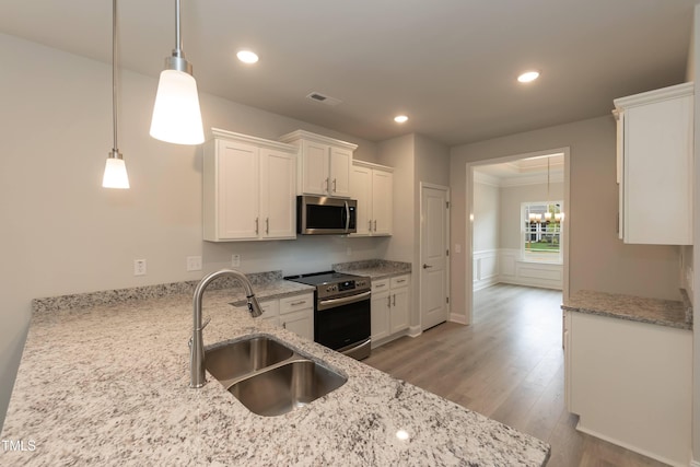 kitchen featuring sink, appliances with stainless steel finishes, pendant lighting, light stone countertops, and white cabinets