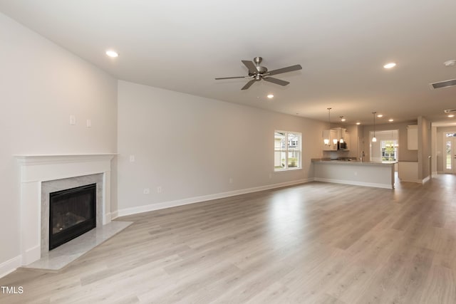 unfurnished living room with a premium fireplace, ceiling fan, and light hardwood / wood-style flooring