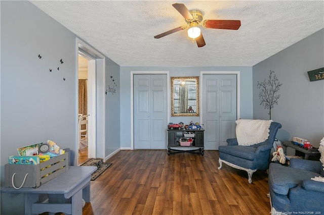 living area with ceiling fan, dark wood-type flooring, and a textured ceiling