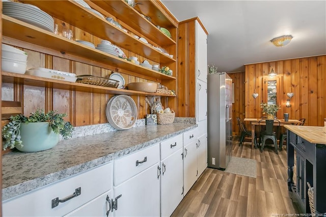 kitchen with wooden walls, stainless steel fridge, light stone countertops, light hardwood / wood-style floors, and white cabinets