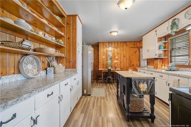 kitchen with wooden walls, white cabinets, stove, light stone counters, and light hardwood / wood-style flooring