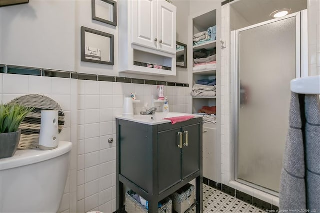 bathroom featuring tile patterned floors, toilet, a shower with shower door, tile walls, and vanity