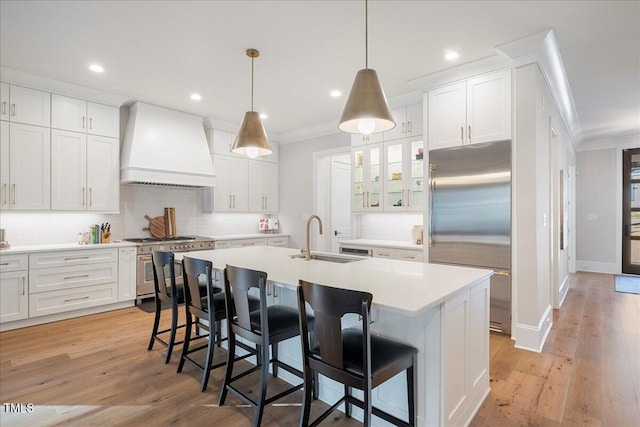 kitchen featuring sink, ornamental molding, high quality appliances, a kitchen island with sink, and wall chimney range hood