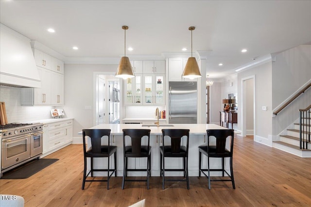 kitchen with high end appliances, white cabinetry, decorative light fixtures, and an island with sink