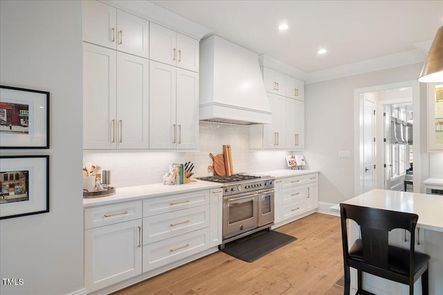 kitchen with range with two ovens, tasteful backsplash, custom range hood, and white cabinets