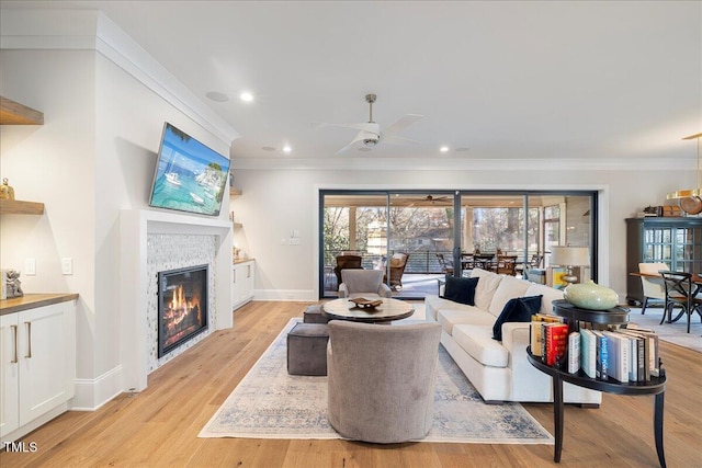 living room featuring ceiling fan, ornamental molding, a fireplace, and light hardwood / wood-style flooring