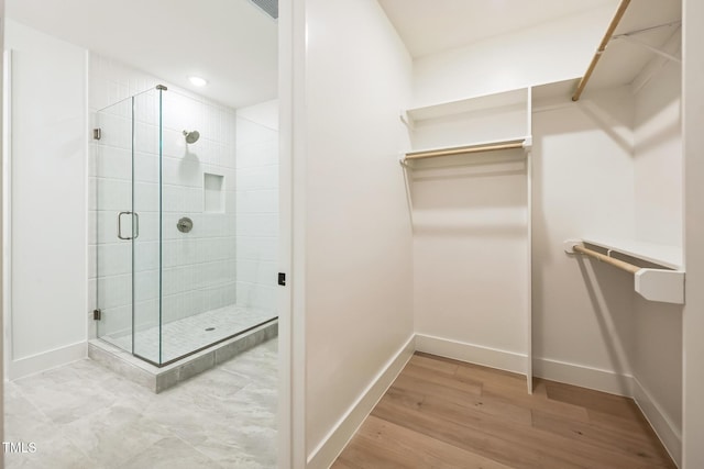 bathroom with a stall shower, a walk in closet, and baseboards