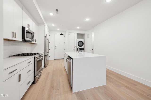 kitchen featuring light wood-type flooring, stacked washer and clothes dryer, modern cabinets, a sink, and stainless steel appliances