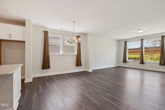 unfurnished dining area featuring a notable chandelier, baseboards, and dark wood-style flooring