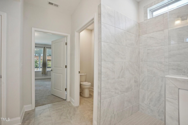 bathroom with toilet, a healthy amount of sunlight, visible vents, and a tile shower