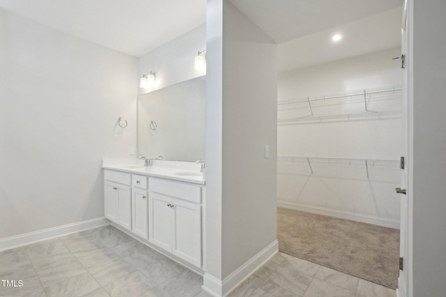 full bath with a walk in closet, a sink, baseboards, and double vanity