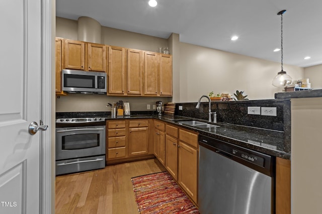 kitchen with pendant lighting, sink, light hardwood / wood-style flooring, appliances with stainless steel finishes, and dark stone countertops