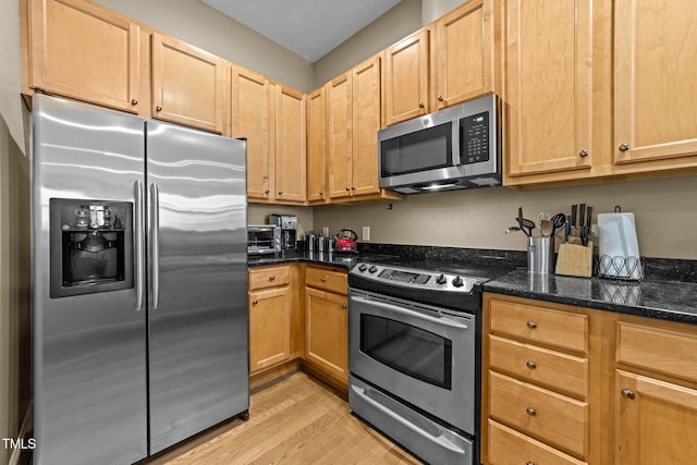 kitchen with dark stone countertops, light hardwood / wood-style flooring, and stainless steel appliances