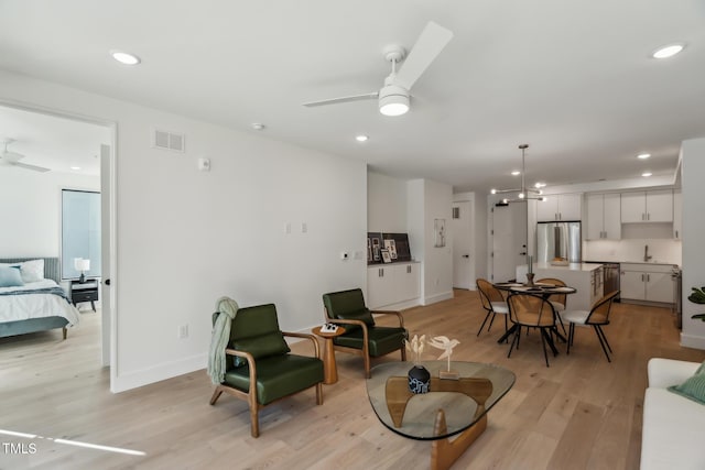 living room with sink, ceiling fan with notable chandelier, and light hardwood / wood-style flooring