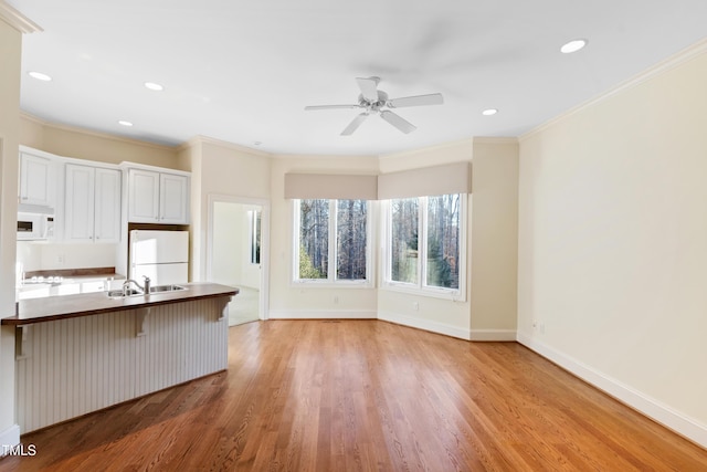 kitchen with white appliances, ornamental molding, a breakfast bar, and white cabinets