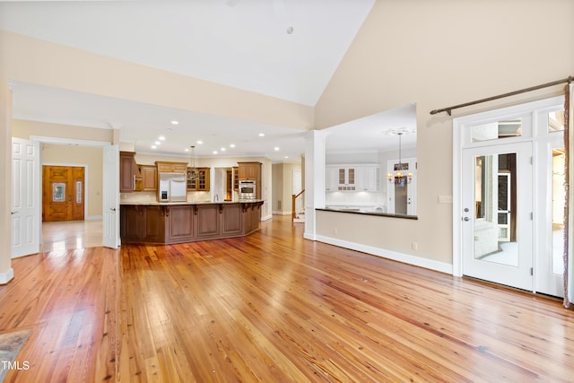 unfurnished living room featuring light wood-type flooring, high vaulted ceiling, and ornate columns