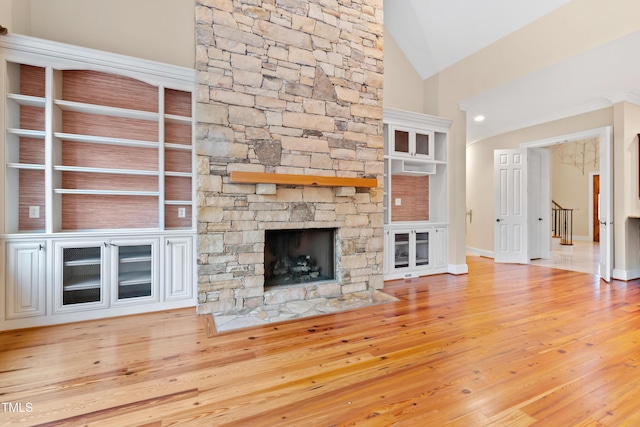 unfurnished living room with lofted ceiling, a stone fireplace, and light wood-type flooring