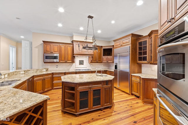 kitchen featuring crown molding, a kitchen island with sink, built in appliances, light stone countertops, and decorative light fixtures