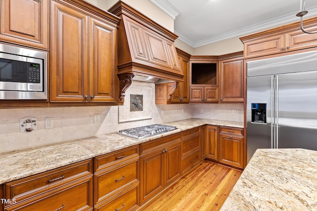 kitchen with premium range hood, decorative backsplash, ornamental molding, built in appliances, and light stone countertops