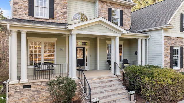 entrance to property with a shingled roof, covered porch, and stone siding