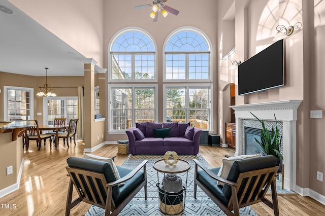 living area with ceiling fan with notable chandelier, a fireplace, and light wood-style flooring