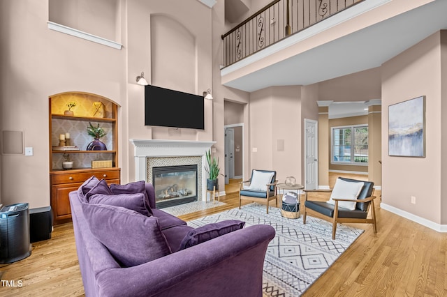 living room with a fireplace, a towering ceiling, light wood-style flooring, and baseboards