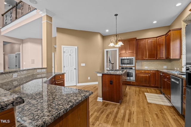 kitchen with light wood-style flooring, stainless steel appliances, backsplash, a center island, and decorative columns