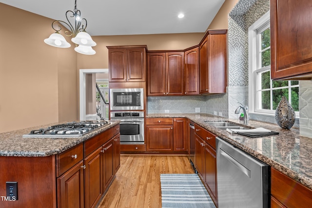 kitchen with tasteful backsplash, a sink, appliances with stainless steel finishes, light wood finished floors, and pendant lighting