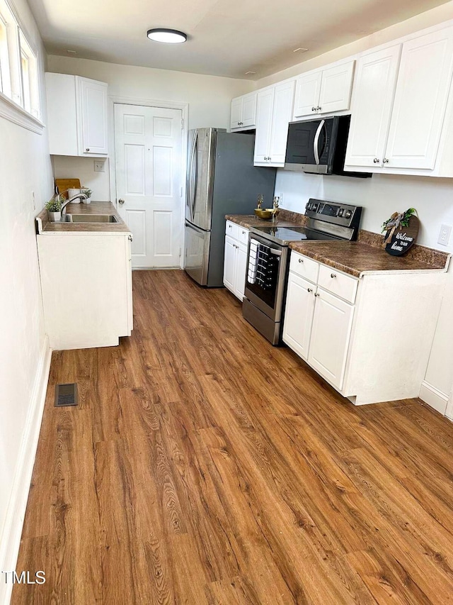 kitchen featuring hardwood / wood-style flooring, stainless steel appliances, sink, and white cabinets