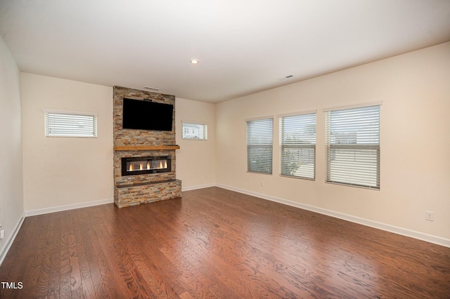 unfurnished living room with a stone fireplace and dark hardwood / wood-style floors