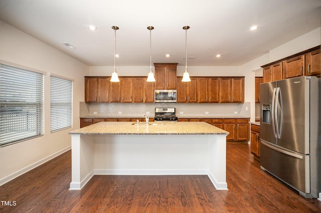 kitchen featuring pendant lighting, sink, a kitchen island with sink, stainless steel appliances, and light stone countertops