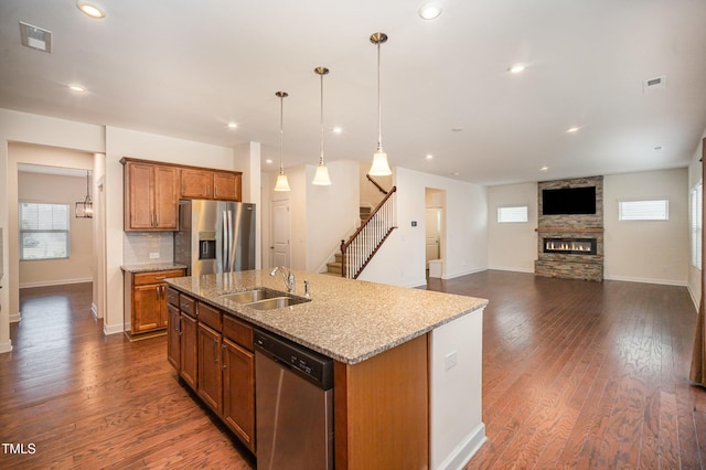 kitchen with sink, hanging light fixtures, appliances with stainless steel finishes, an island with sink, and light stone countertops