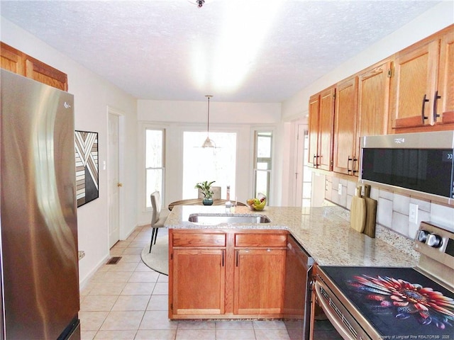 kitchen with pendant lighting, sink, stainless steel appliances, decorative backsplash, and kitchen peninsula