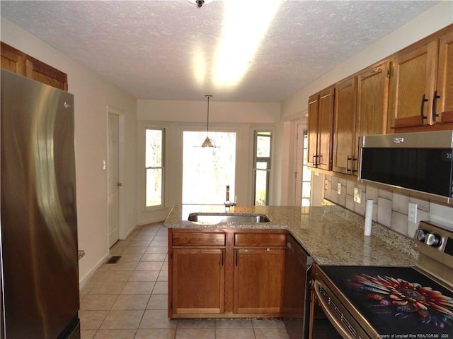 kitchen featuring pendant lighting, sink, appliances with stainless steel finishes, light stone countertops, and kitchen peninsula