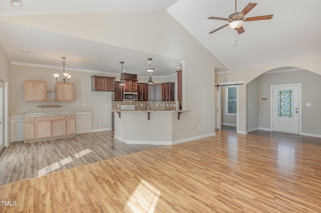 unfurnished living room featuring crown molding, ceiling fan with notable chandelier, high vaulted ceiling, and light hardwood / wood-style flooring