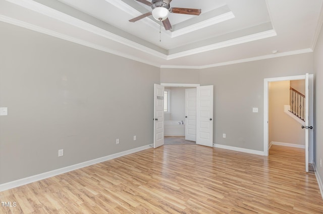 unfurnished bedroom featuring ensuite bath, ceiling fan, ornamental molding, a raised ceiling, and light wood-type flooring