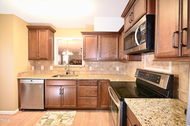 kitchen with stainless steel appliances, light stone countertops, sink, and light hardwood / wood-style flooring