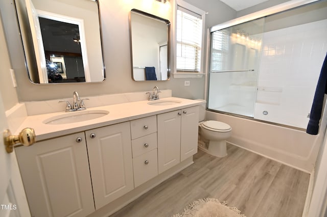 full bathroom featuring hardwood / wood-style flooring, vanity, shower / bath combination with glass door, and toilet