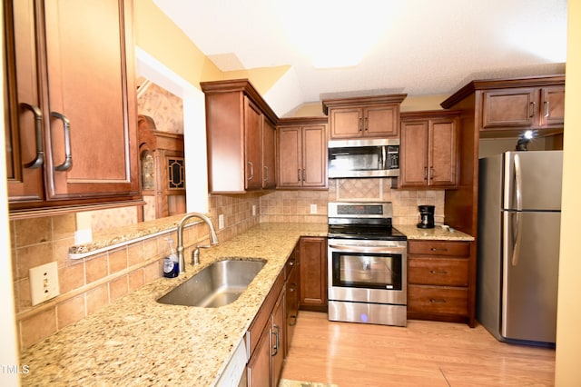 kitchen with appliances with stainless steel finishes, sink, backsplash, light stone counters, and light hardwood / wood-style flooring