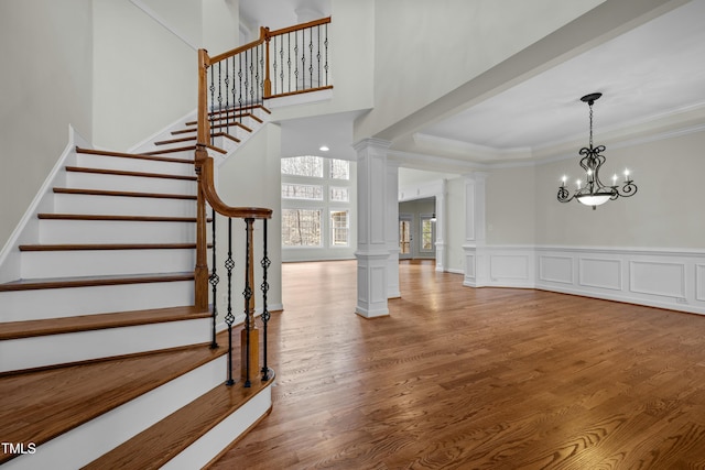 staircase featuring a notable chandelier, ornamental molding, ornate columns, and wood finished floors