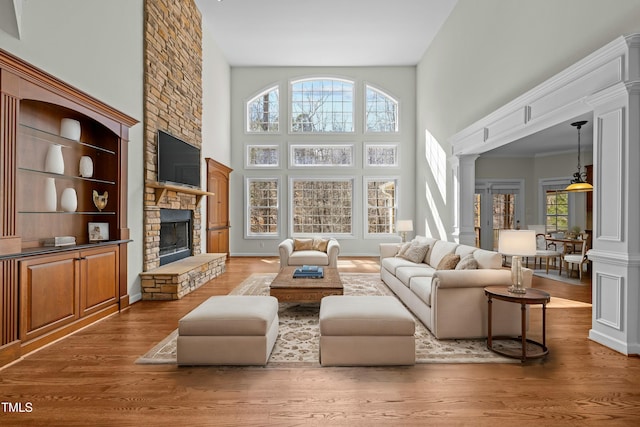 living room featuring a stone fireplace, a high ceiling, ornate columns, and wood finished floors