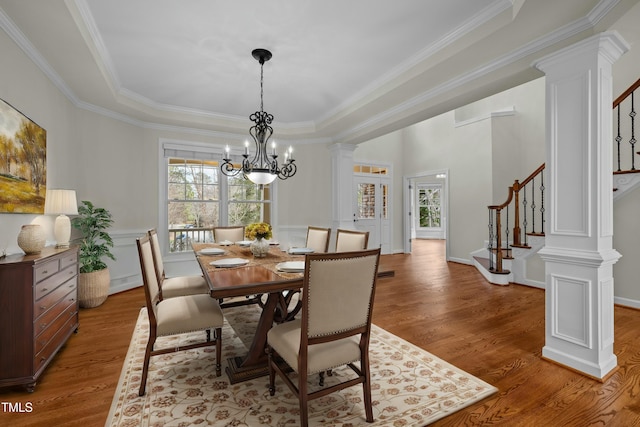 dining area with ornamental molding, wood finished floors, an inviting chandelier, stairs, and ornate columns